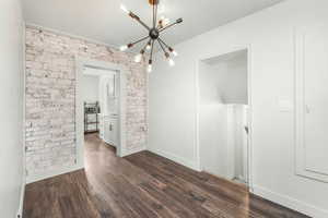 Unfurnished dining area featuring a chandelier, brick wall, dark wood-style flooring, and baseboards