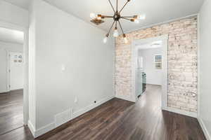 Unfurnished room with dark wood-type flooring, baseboards, visible vents, and brick wall