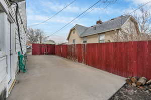 View of side of home with roof with shingles, a chimney, a patio area, and fence