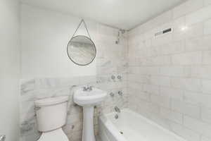 Bathroom with visible vents, tile walls, toilet, and bathing tub / shower combination