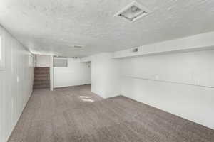 Carpeted spare room featuring a textured ceiling, stairway, and visible vents