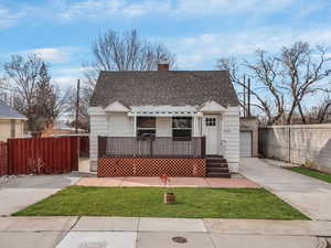 Bungalow-style home featuring a fenced front yard, a chimney, a shingled roof, and concrete driveway