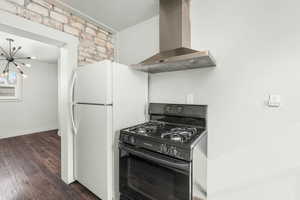 Kitchen with dark wood-style floors, freestanding refrigerator, an inviting chandelier, island exhaust hood, and black range with gas stovetop