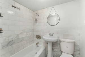 Full bathroom with toilet, shower / tub combination, visible vents, and tile walls