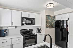 Kitchen featuring tasteful backsplash, white cabinets, a textured ceiling, and black appliances