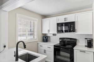 Kitchen featuring white cabinetry, sink, decorative backsplash, and black appliances