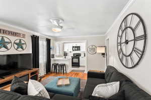 Living room with crown molding, ceiling fan, and light wood-type flooring