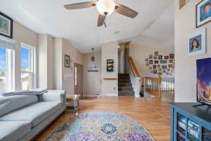 Living room with lofted ceiling, stairway, a ceiling fan, wood finished floors, and baseboards