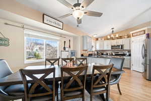 Dining room with vaulted ceiling, ceiling fan with notable chandelier, and light wood-style floors