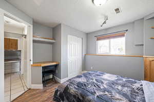 Bedroom featuring baseboards, visible vents, dark wood finished floors, a textured wall, and a textured ceiling