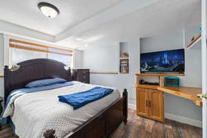 Bedroom featuring a textured ceiling, a textured wall, dark wood-style flooring, baseboards, and built in desk