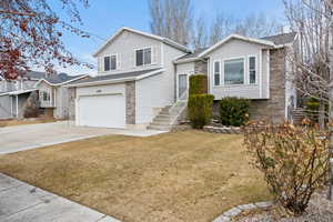 Tri-level home with concrete driveway, brick siding, a front lawn, and an attached garage