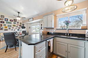 Kitchen with dark stone counters, dishwasher, a peninsula, light wood-style floors, and a sink