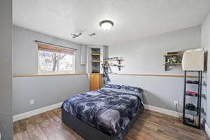 Bedroom featuring baseboards, visible vents, dark wood finished floors, and a textured wall