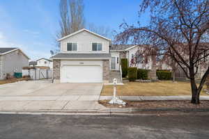 Split level home with brick siding, a front yard, fence, a garage, and driveway