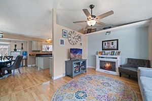 Living area with a warm lit fireplace, baseboards, ceiling fan, vaulted ceiling, and light wood-style floors