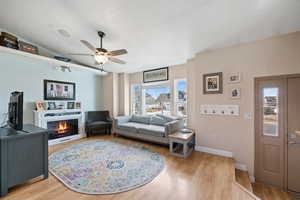 Living area featuring ceiling fan, a textured ceiling, baseboards, a lit fireplace, and light wood finished floors