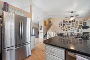 Kitchen featuring appliances with stainless steel finishes, light wood-style floors, white cabinets, vaulted ceiling, and dark stone counters