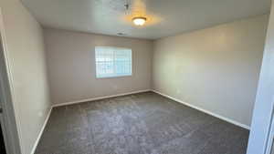 Empty room featuring dark carpet, a textured ceiling, baseboards, and a pendent fire sprinkler