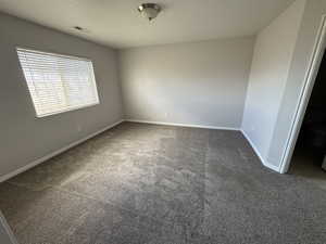 Unfurnished bedroom featuring baseboards, dark colored carpet, a textured ceiling, and visible vents
