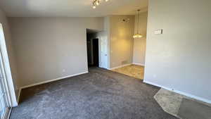 Spare room featuring vaulted ceiling, carpet, baseboards, and a chandelier