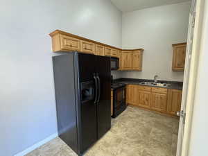 Kitchen featuring black appliances, brown cabinetry, dark countertops, and a sink