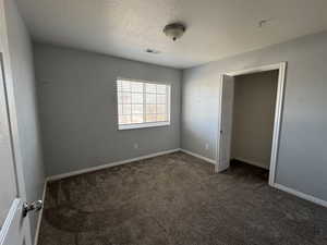 Unfurnished bedroom featuring dark colored carpet, visible vents, a textured ceiling, and baseboards