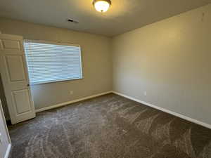 Empty room with a textured ceiling, dark colored carpet, visible vents, and baseboards