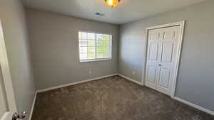 Unfurnished bedroom with dark colored carpet and baseboards