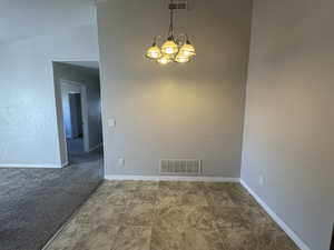 Unfurnished room featuring carpet floors, visible vents, a notable chandelier, and baseboards