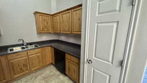 Kitchen featuring black dishwasher, a sink, dark countertops, and brown cabinets