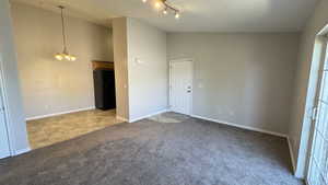 Carpeted spare room with a chandelier, vaulted ceiling, and baseboards