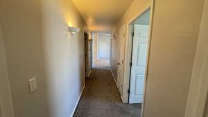 Hallway featuring dark colored carpet, baseboards, and a textured ceiling