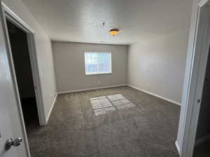 Spare room with dark carpet, a textured ceiling, and baseboards