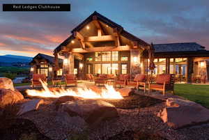 Back of house at dusk featuring stone siding, a patio, and an outdoor living space with a fire pit