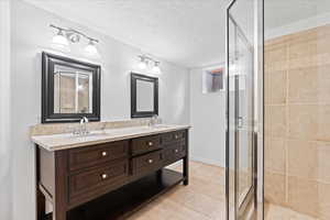 Full bath with a textured ceiling, double vanity, a stall shower, and a sink