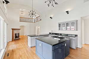 Kitchen featuring a center island, arched walkways, stainless steel gas cooktop, dark countertops, and glass insert cabinets