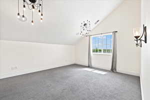 Bedroom with adjoining bathroom, inviting chandeliers, vaulted ceiling, and carpet flooring