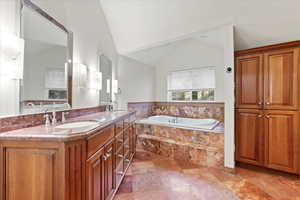 Bathroom with lofted ceiling, double vanity, a sink, and a bath