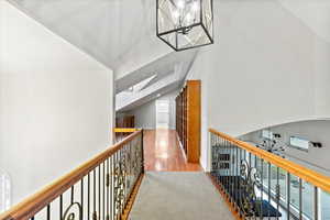 Hall featuring light wood-style floors, lofted ceiling with skylight, and a notable chandelier