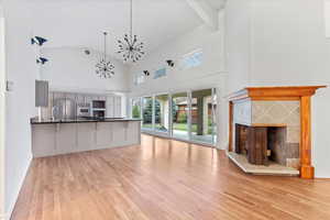 Unfurnished living room with a notable chandelier, vaulted ceiling, light wood-style floors, a fireplace, and a sink