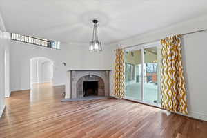 Unfurnished living room featuring arched walkways, baseboards, a tile fireplace, light wood-style flooring, and crown molding