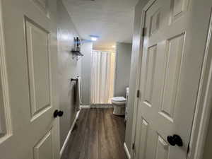 Bathroom with baseboards, a textured ceiling, toilet, and wood finished floors