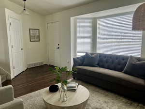 Living area with dark wood-style flooring, visible vents, baseboards, vaulted ceiling, and stairway