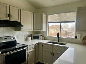 Kitchen featuring tasteful backsplash, light countertops, appliances with stainless steel finishes, a sink, and under cabinet range hood