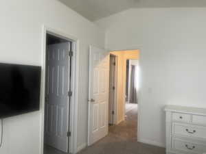 Hallway featuring lofted ceiling, baseboards, and dark carpet