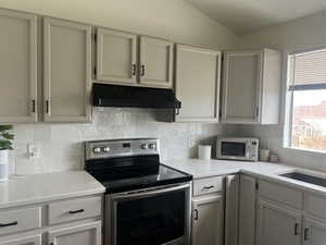 Kitchen featuring appliances with stainless steel finishes, light countertops, decorative backsplash, and exhaust hood