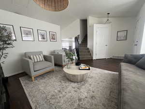 Living area featuring dark wood-type flooring, visible vents, baseboards, vaulted ceiling, and stairway