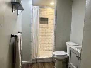 Full bath featuring a textured wall, a stall shower, wood finished floors, and toilet