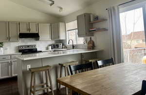 Kitchen featuring decorative backsplash, a breakfast bar area, stainless steel appliances, light countertops, and under cabinet range hood